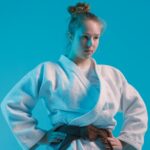 girl judoka in a white kimano with a black belt on a blue background, studio photo