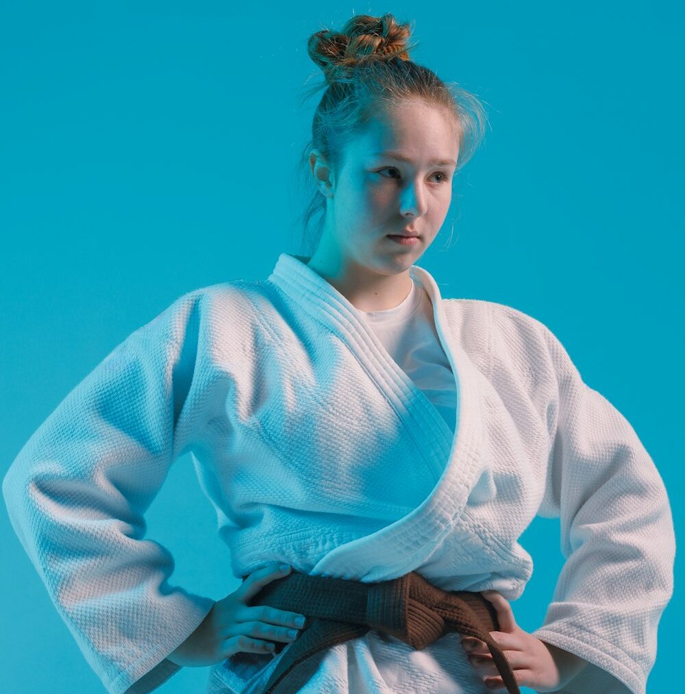 girl judoka in a white kimano with a black belt on a blue background, studio photo